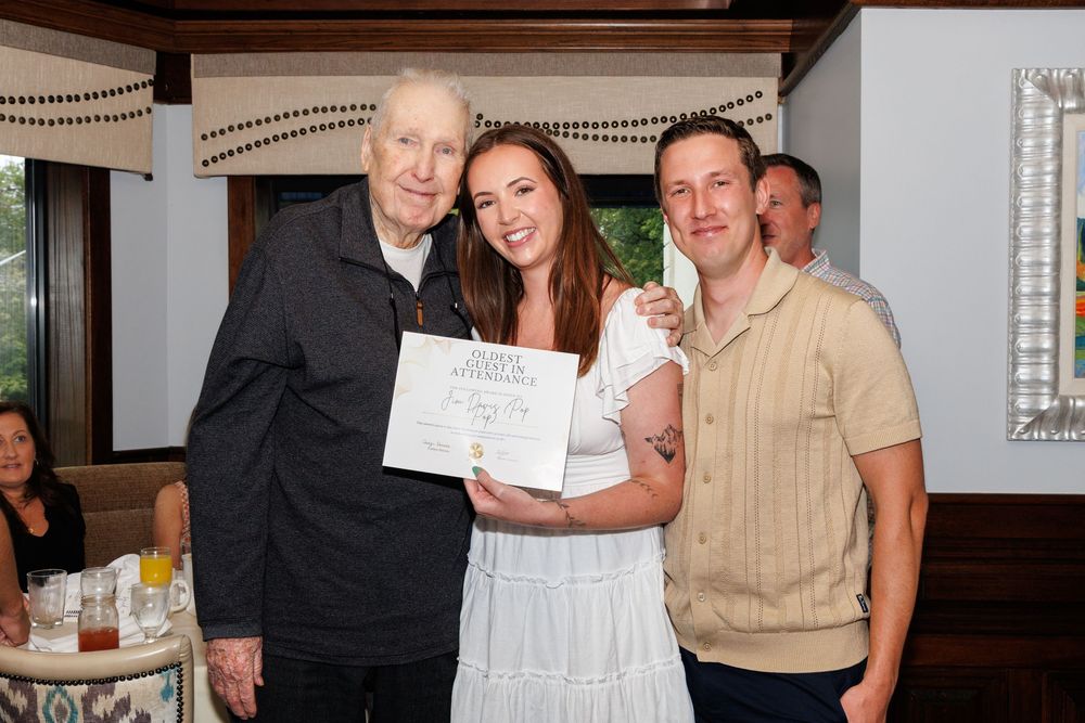 Indoor celebration with people gathered around displaying documents and certificates.