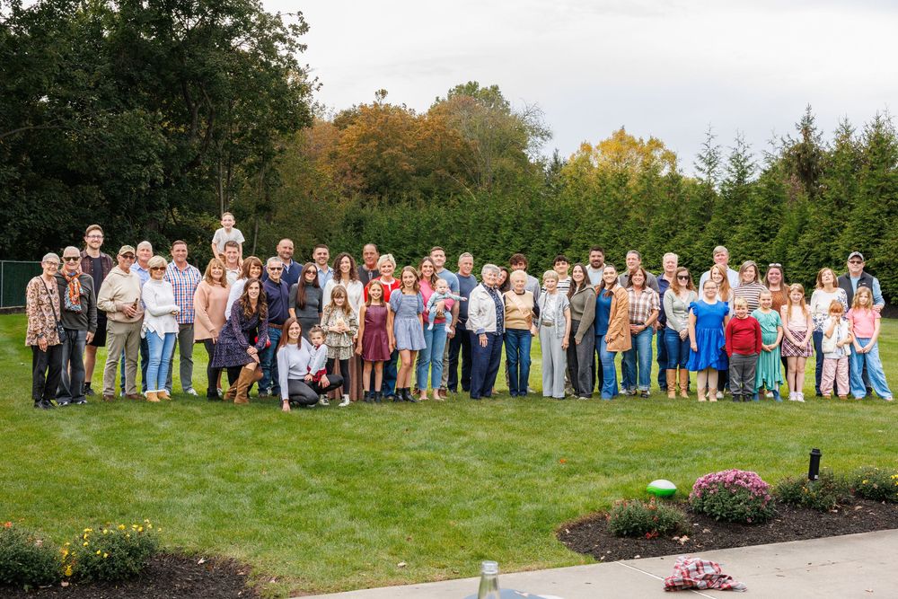 Large group photo of party attendees lined up outdoors on a grassy hillside.