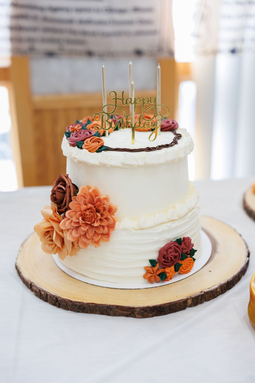 White wedding cake decorated with orange dahlias and floral accents on a rustic wood slice base.