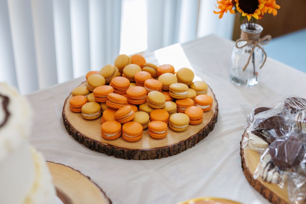 Orange macarons and desserts displayed on a white tablecloth at a celebration.