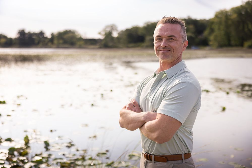 Person in white shirt smiling and enjoying a peaceful moment by a serene lake at sunset.