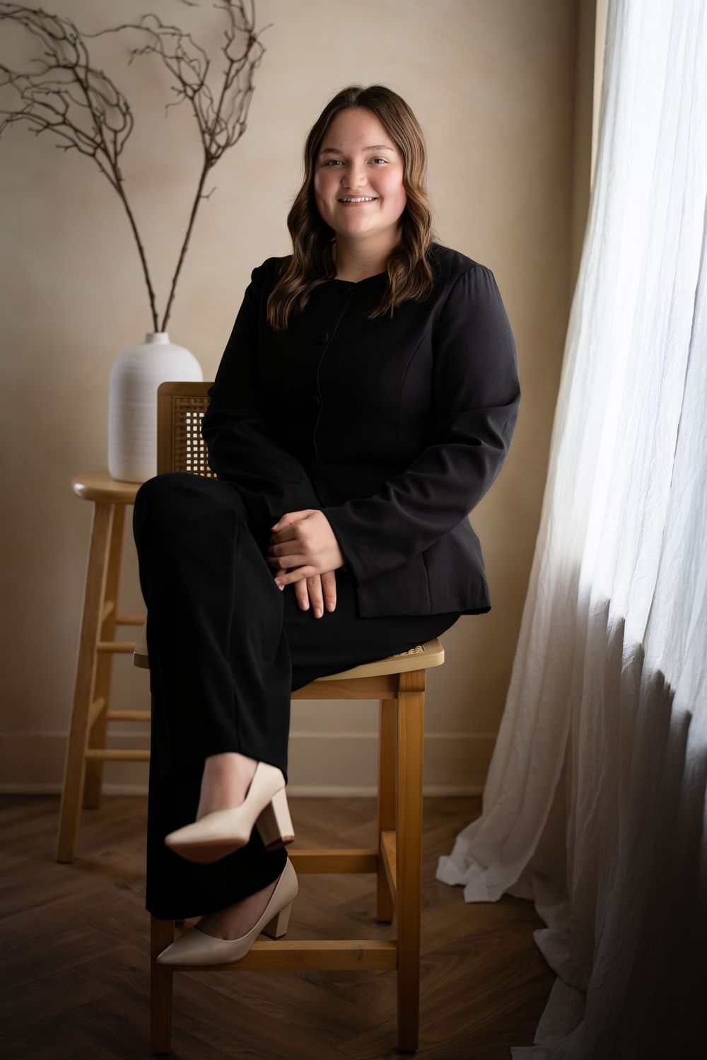 A series of four photos showing someone in a black sweater dress posing on a wooden chair near a window.
