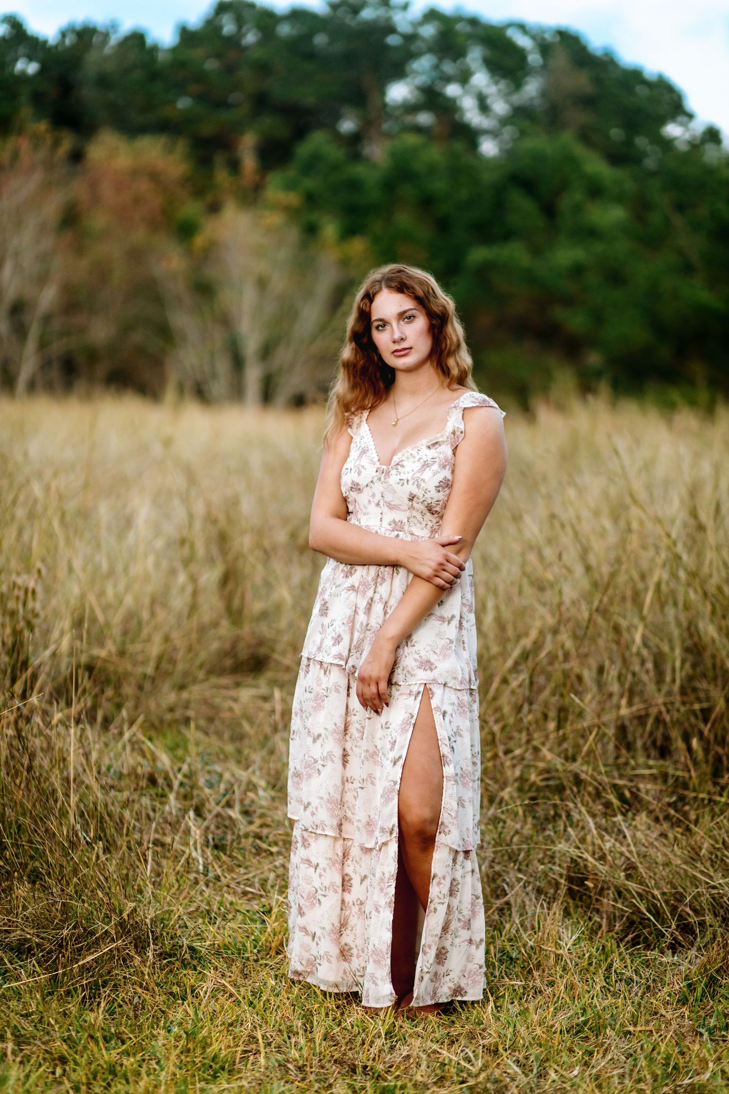 A floral sundress flows in the tall golden grass of a sunlit meadow with trees in the background.
