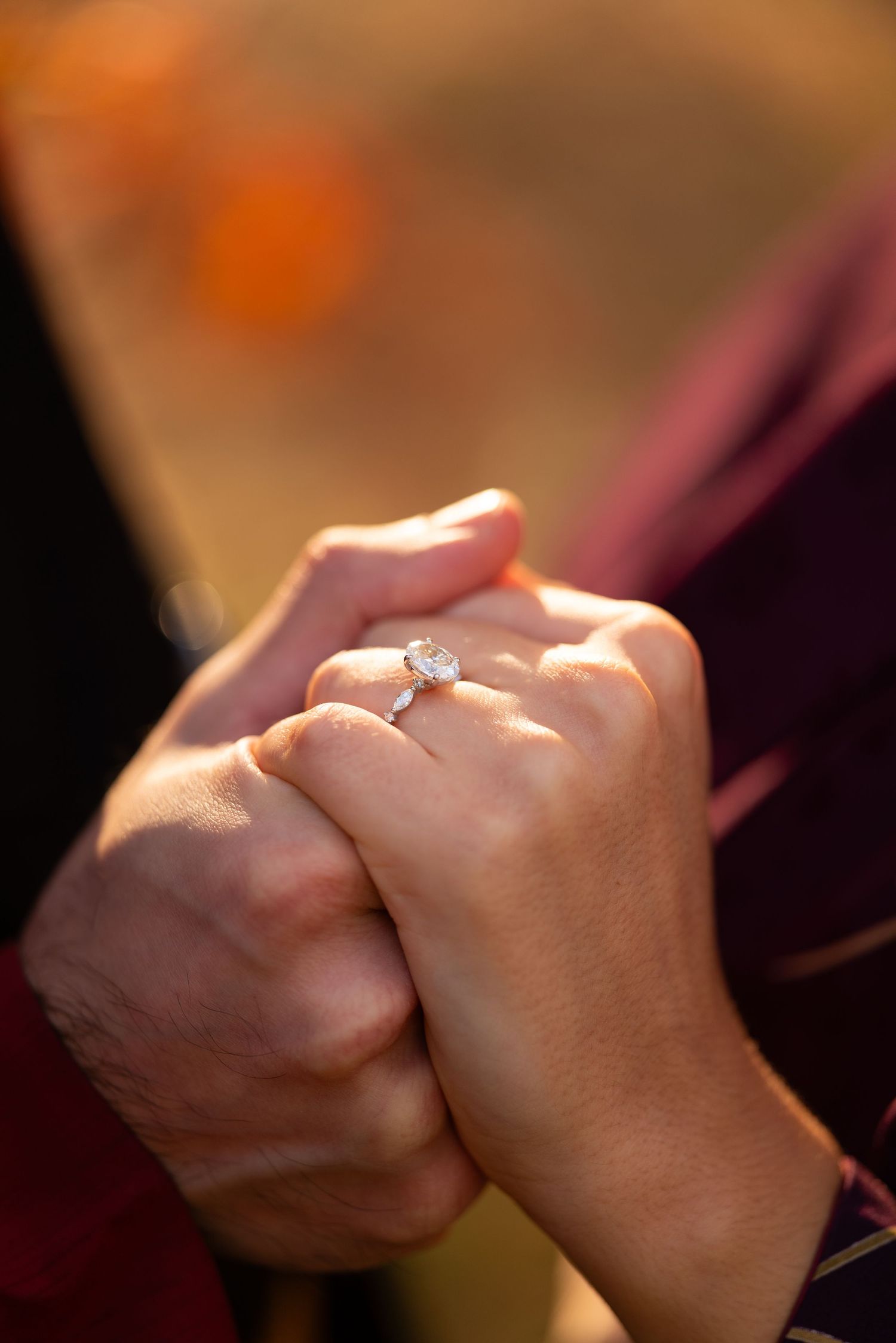 Close-up of an engagement ring on a woman's hand held tenderly by her partner in red kimono.