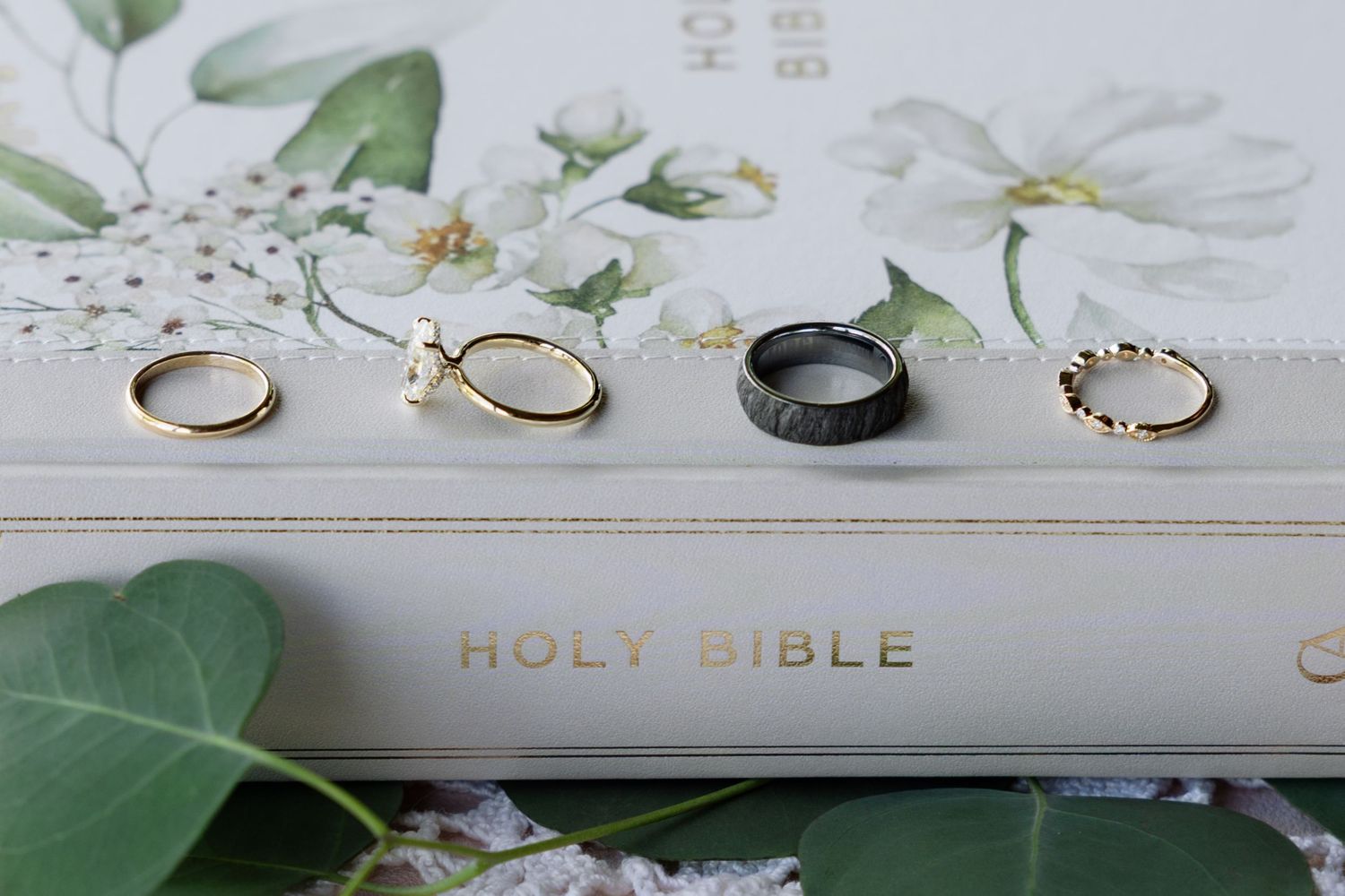 A collage of wedding details including rings, flowers, and a Holy Bible arranged on white surfaces.