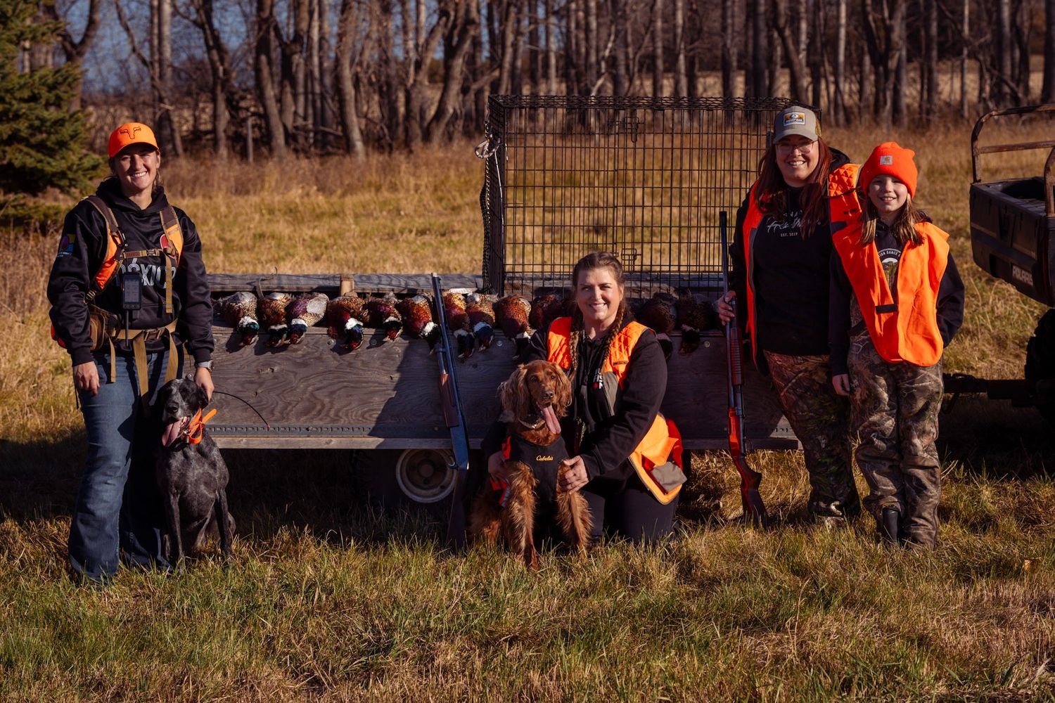 A group of hunters in orange safety vests gather outdoors during hunting season.