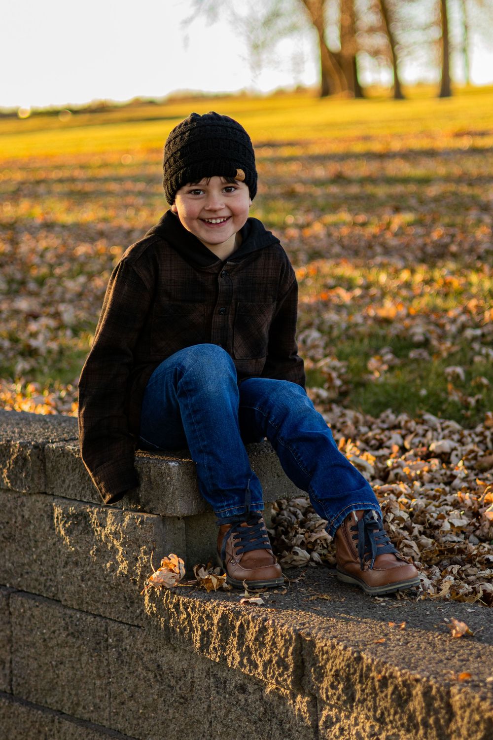 Child relaxes on concrete wall during golden hour with autumn foliage in background.
