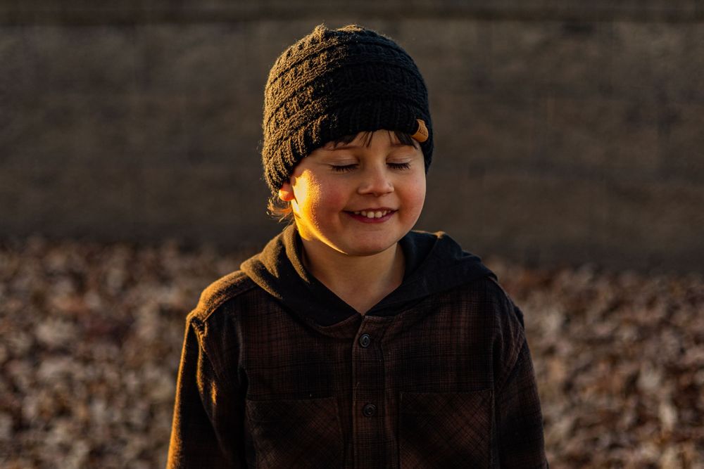 Close-up portrait in warm sunset lighting showing person in dark hoodie and knit cap.