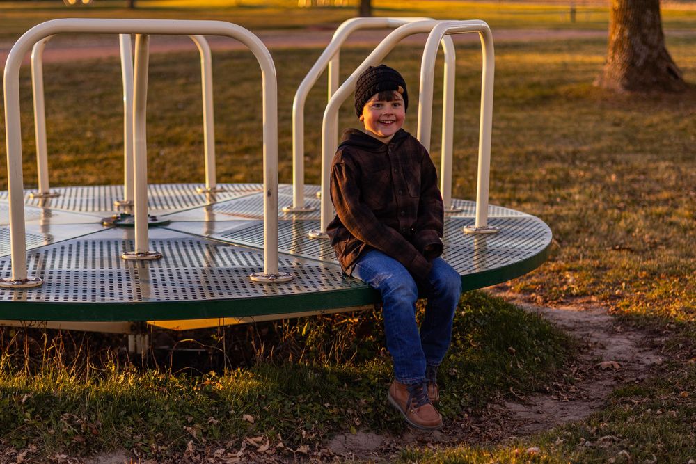 Person in winter attire sits on metal playground equipment at dusk.