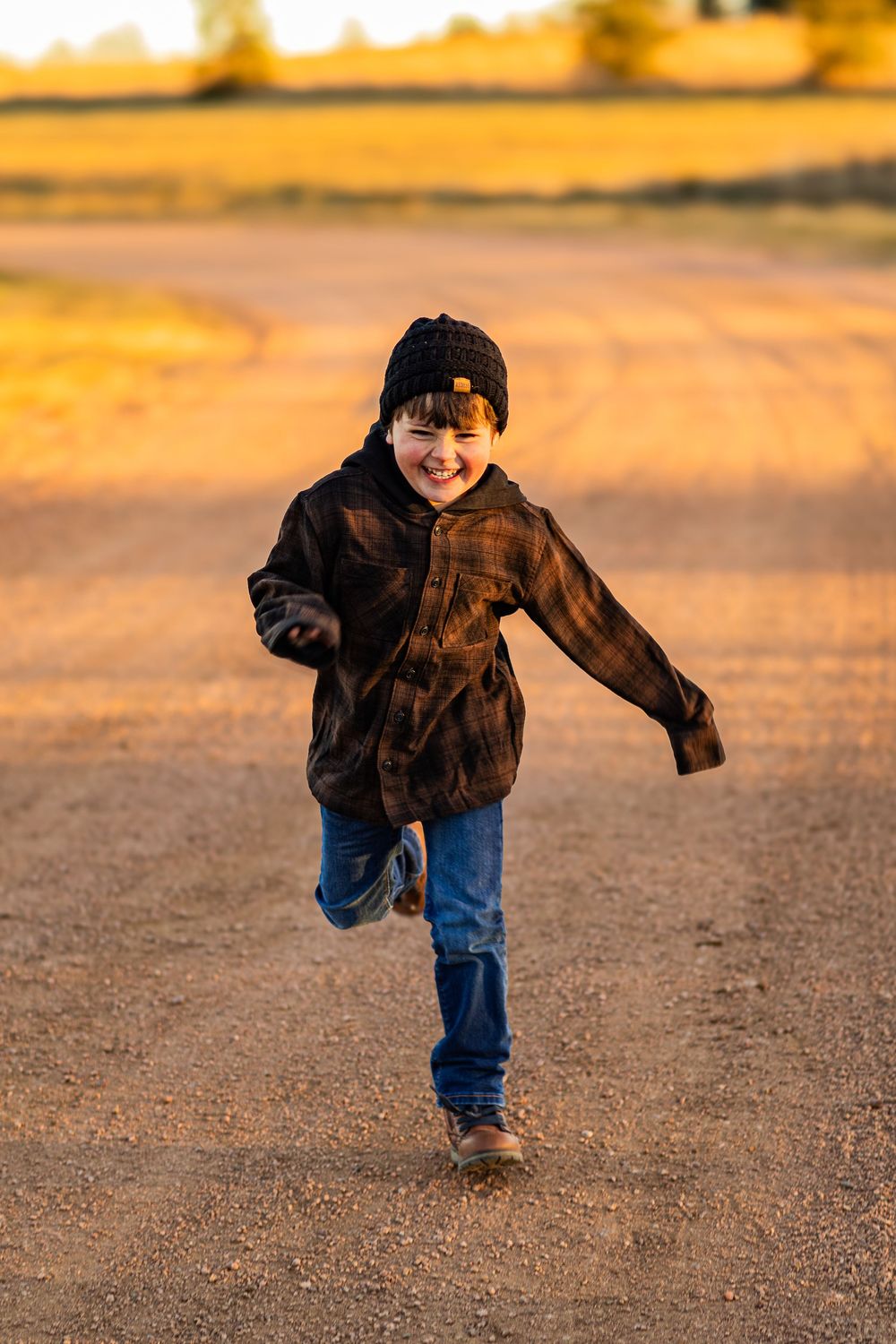 Person in dark hoodie and jeans runs along dirt path during golden hour.