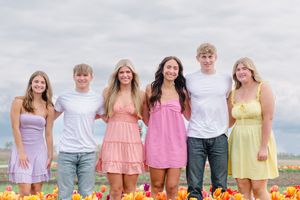 A group stands together outdoors in pastel colored summer outfits against a bright sky and field.