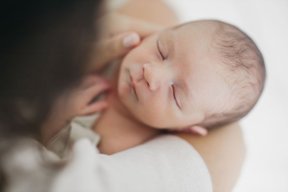Sleeping newborn baby wrapped in soft white blanket being gently cradled in arms.