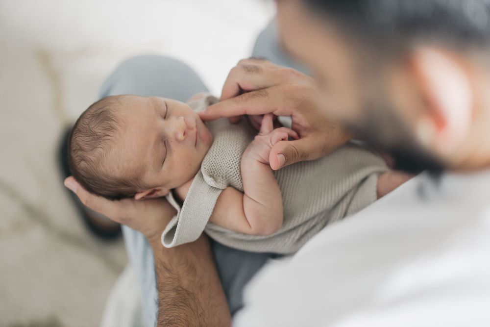 Tender moment as hands cradle sleeping newborn baby in white blanket.