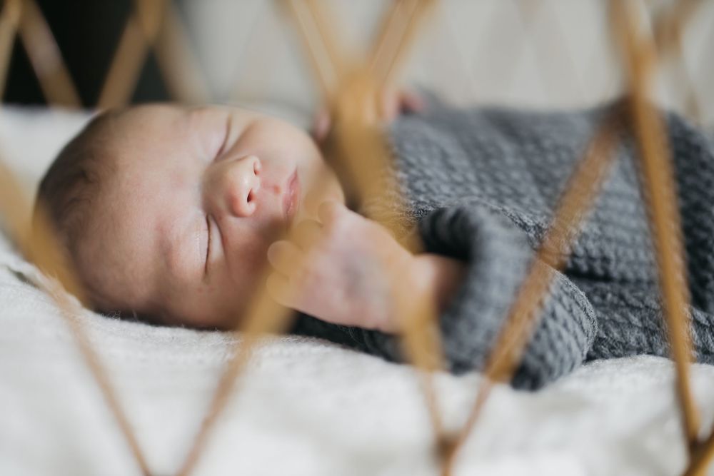 Peaceful newborn baby resting on gray blanket while being comforted by gentle hands.