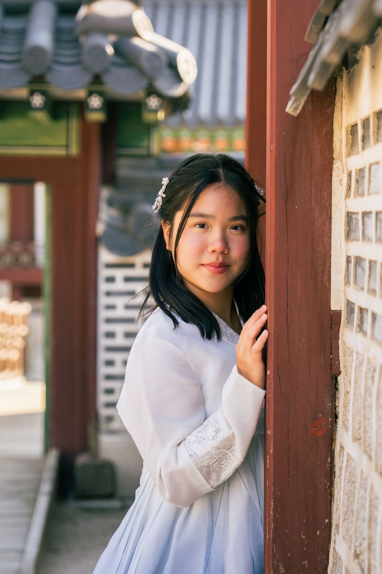 A person in traditional Korean hanbok dress poses along a wooden corridor of a traditional building.