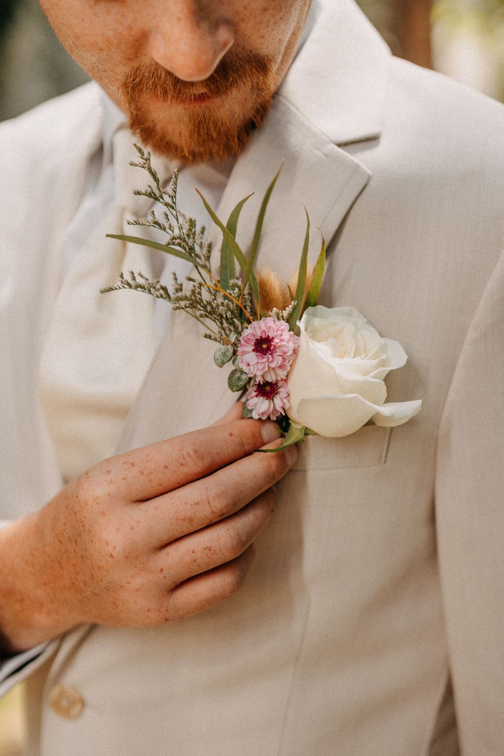 Three close-up photos show a boutonniere with pink and white flowers being pinned to a white suit lapel.