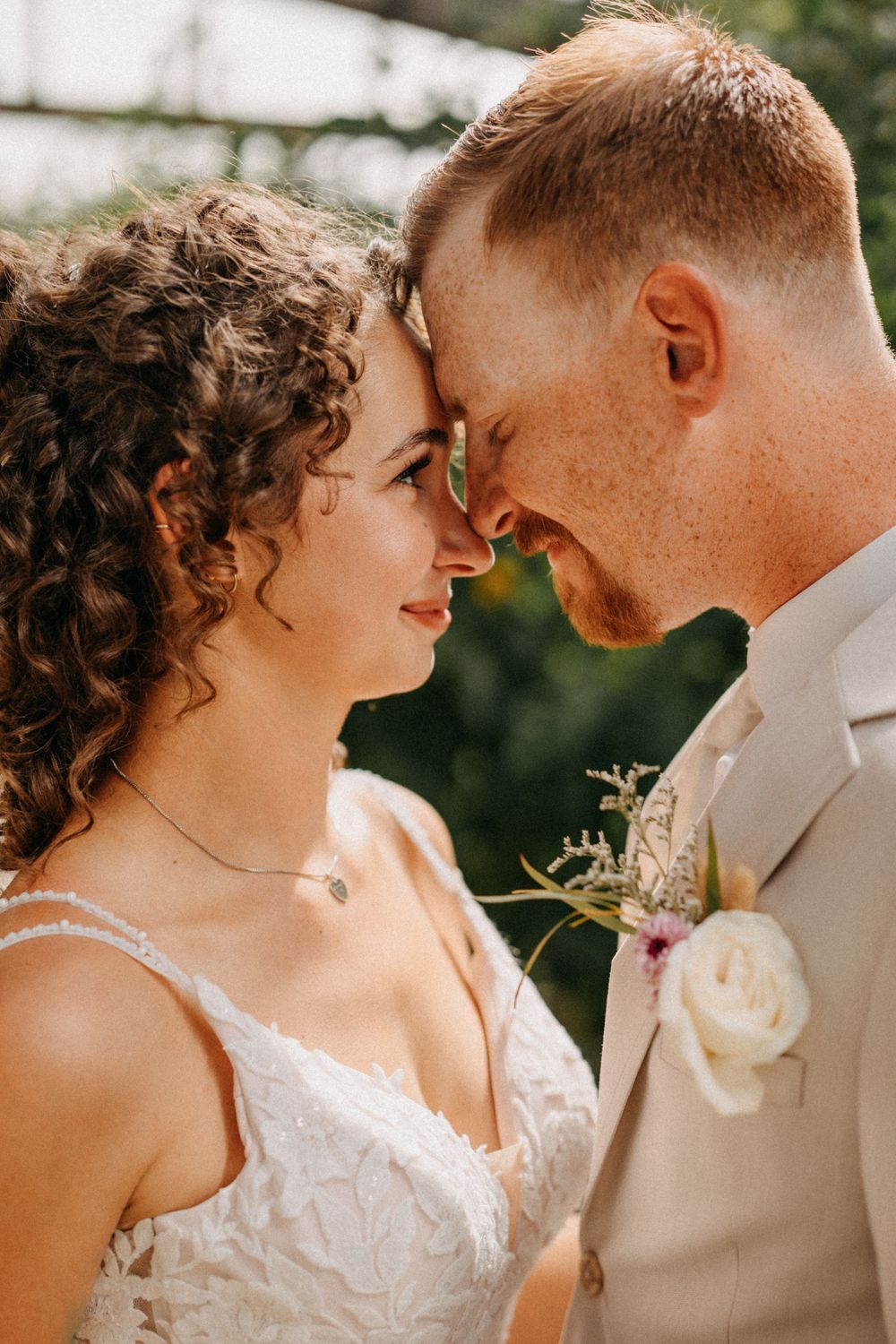 A tender moment between newlyweds as they touch foreheads in warm sunlight.