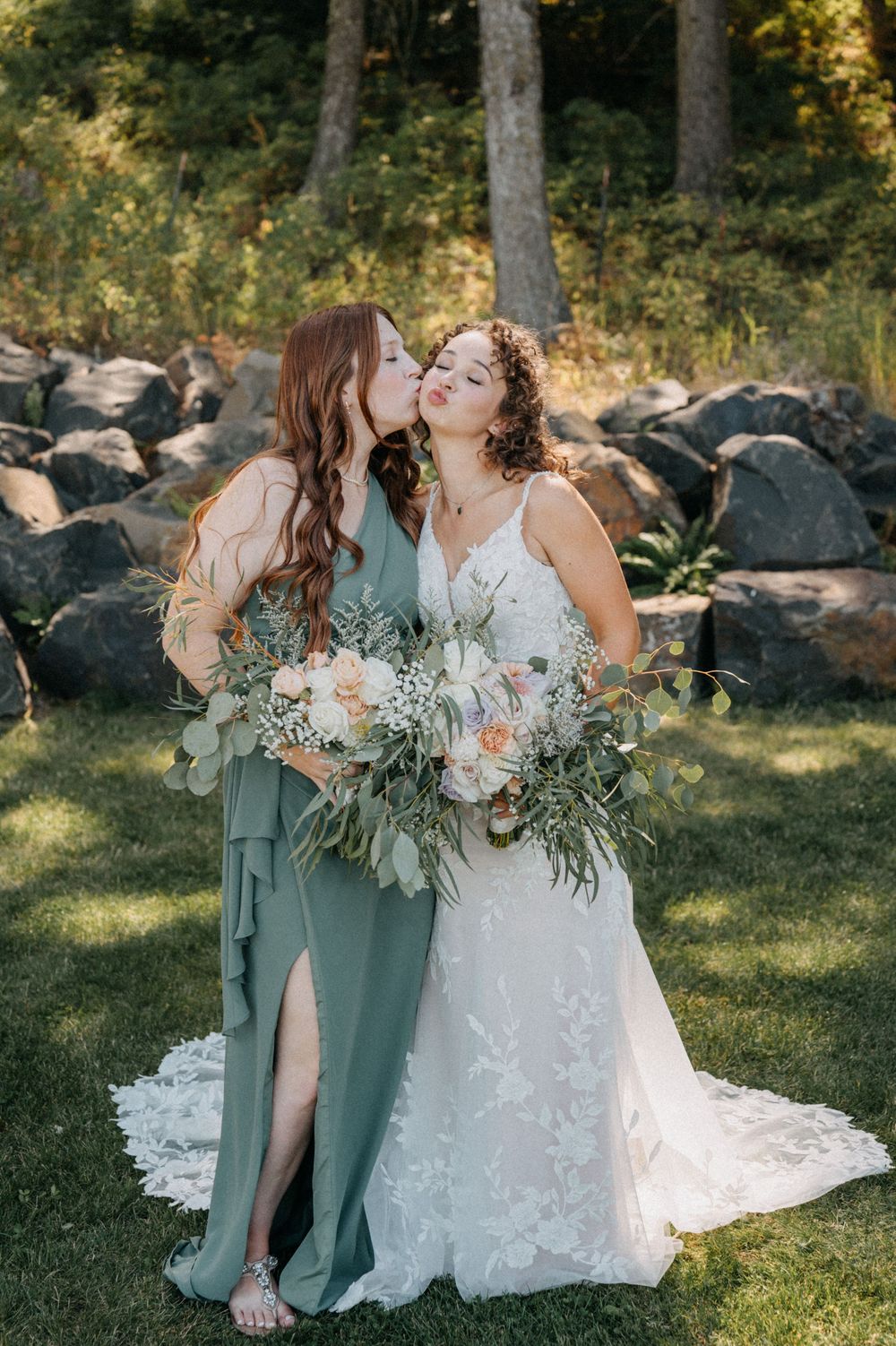 Bridesmaids in sage green dresses pose with bride in lace gown during outdoor woodland wedding photoshoot.