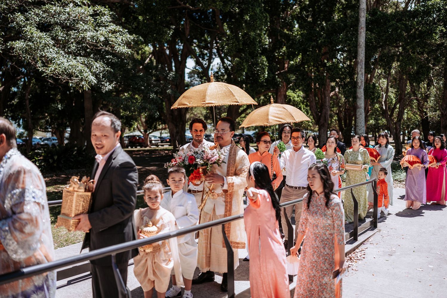 Wedding procession walking along a path with parasols and colorful attire.