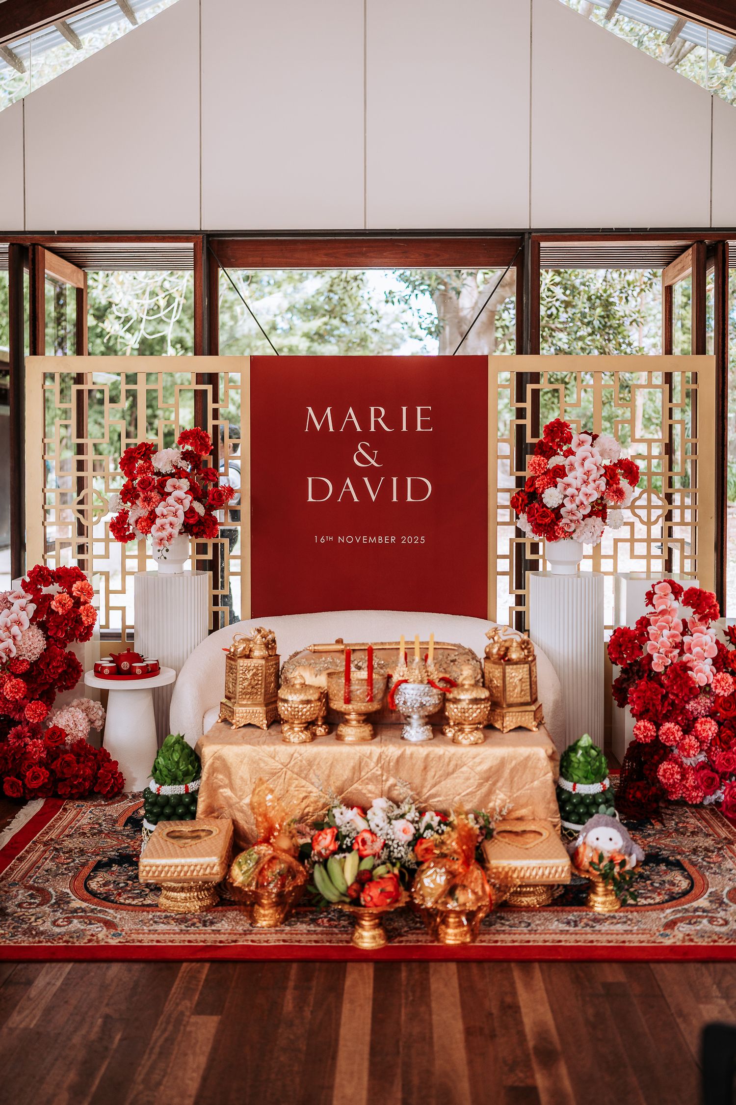 Elegant wedding reception setup with burgundy backdrop, gold decor, and cascading red roses creating a romantic atmosphere.