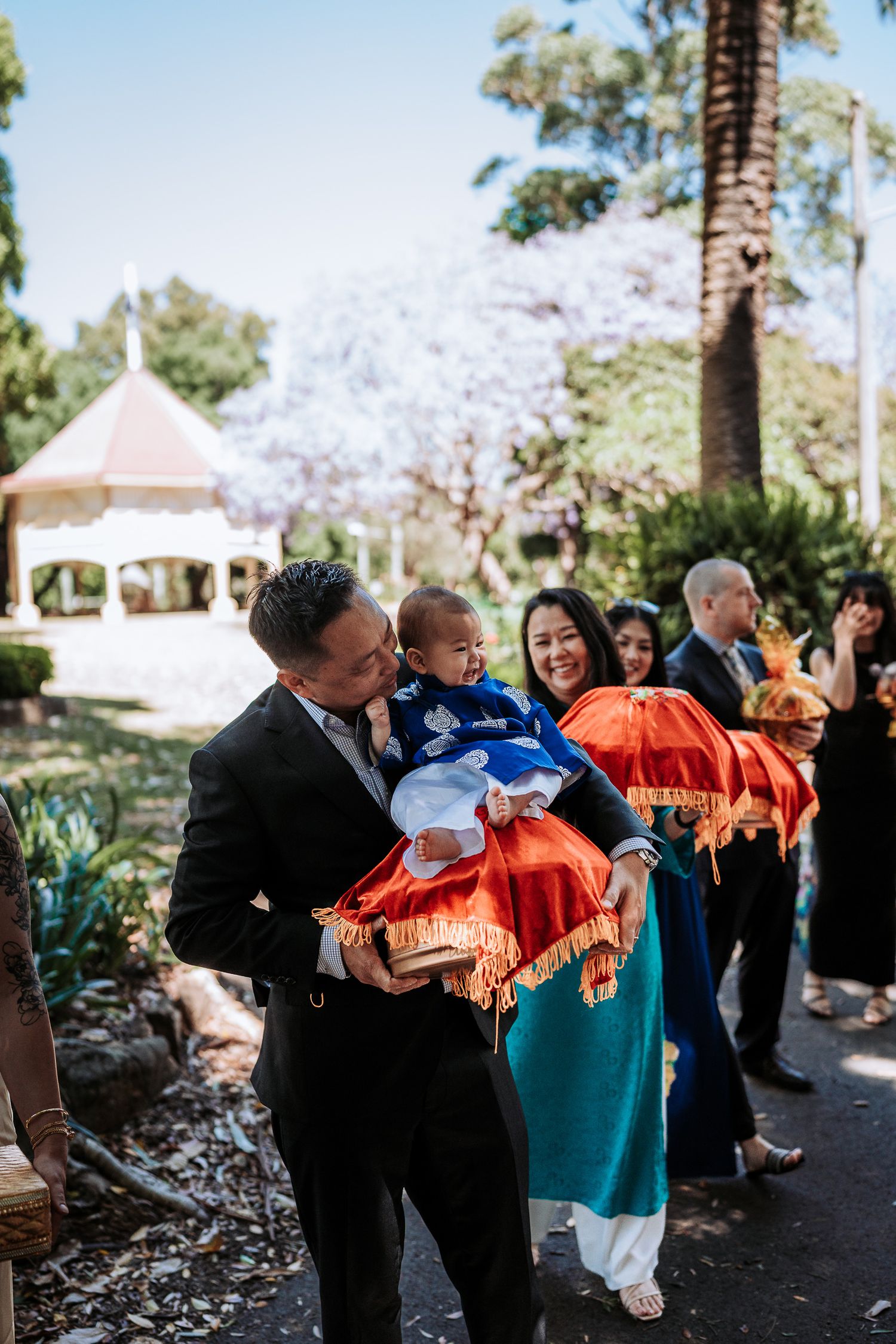 Guests at an outdoor wedding ceremony share blankets and shawls on a sunny day.