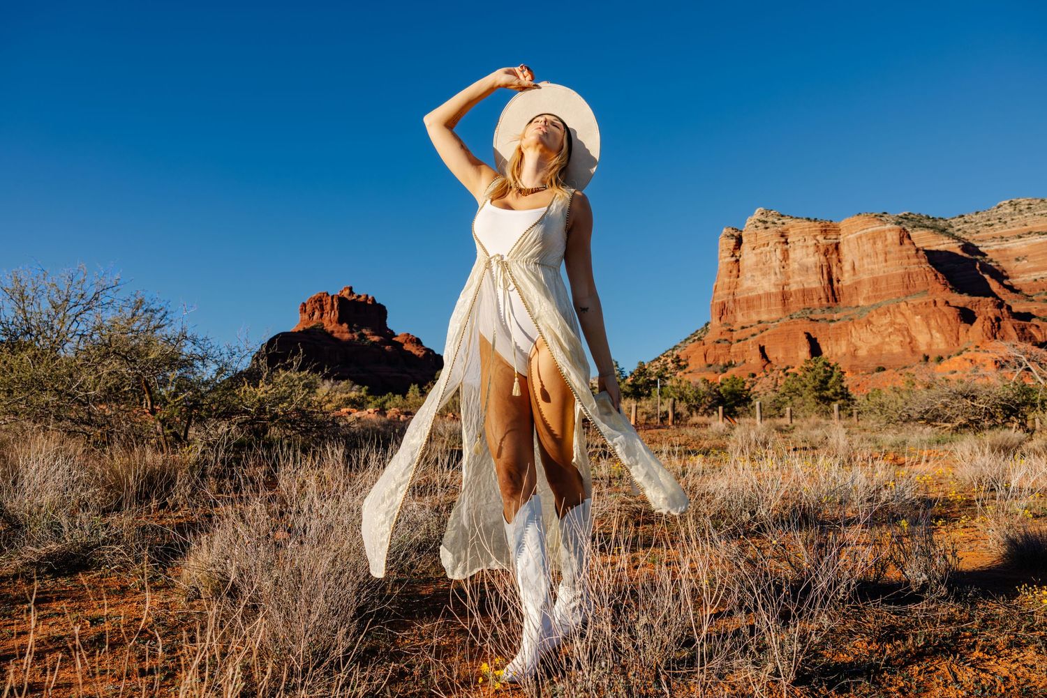 A figure in a flowing white dress stands gracefully against the backdrop of red rock formations in the desert landscape.