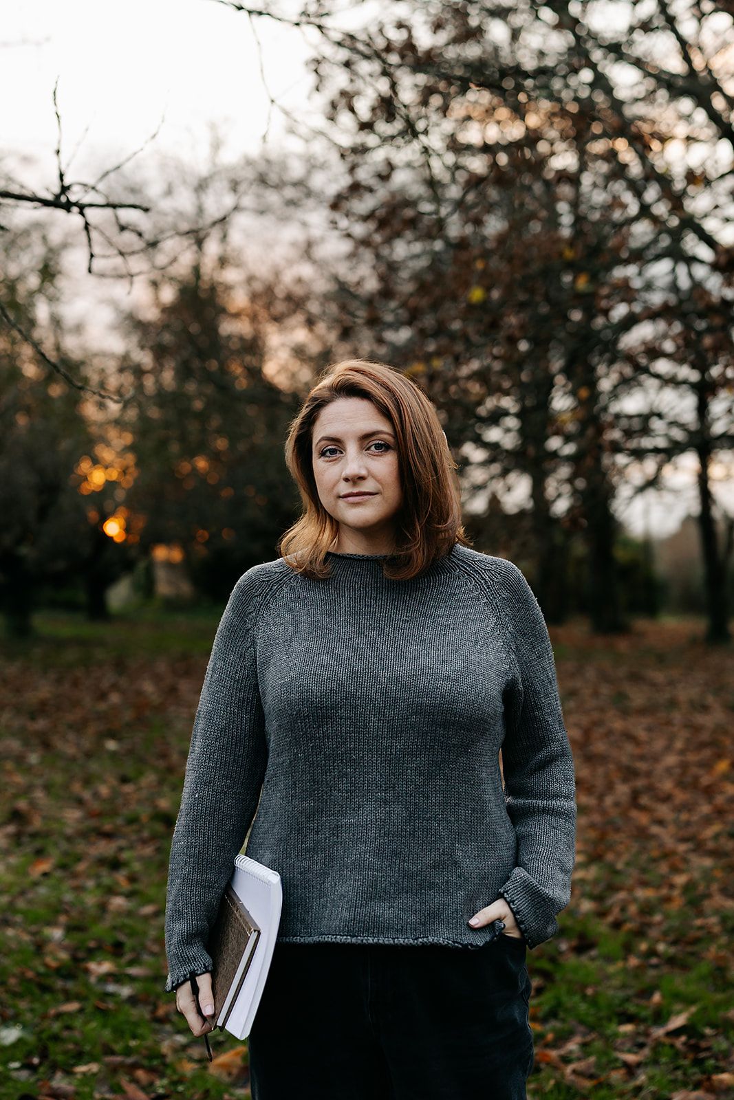 A series of photos showing someone wearing a gray sweater holding a book while standing in an autumn park setting at dusk.