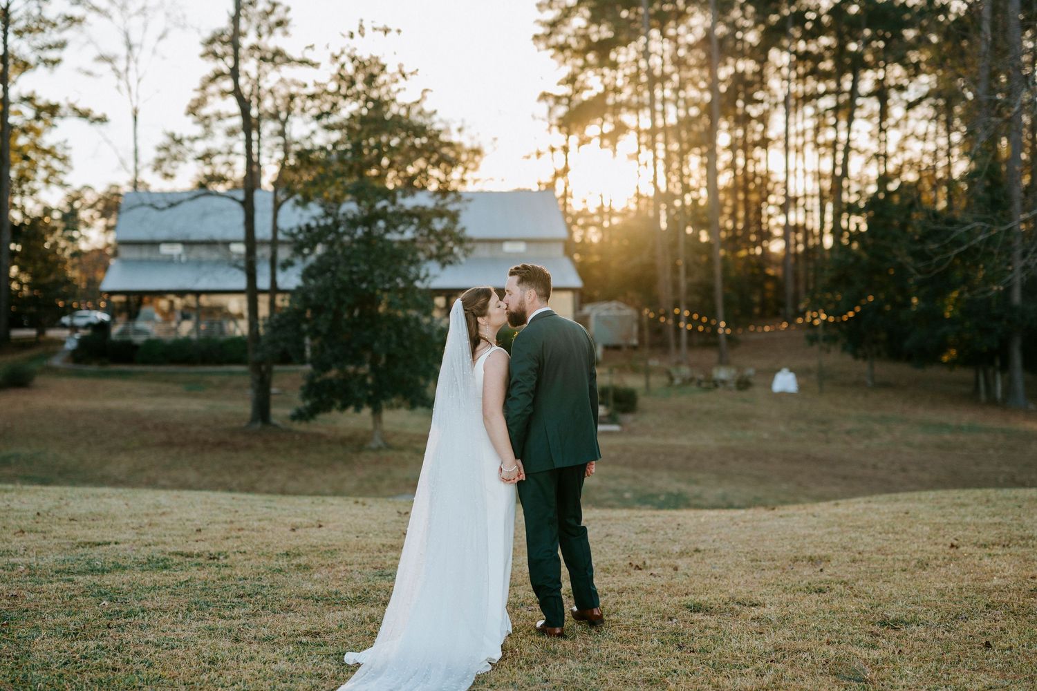 Couple walks hand in hand through a sunlit pine forest during golden hour at their outdoor wedding.