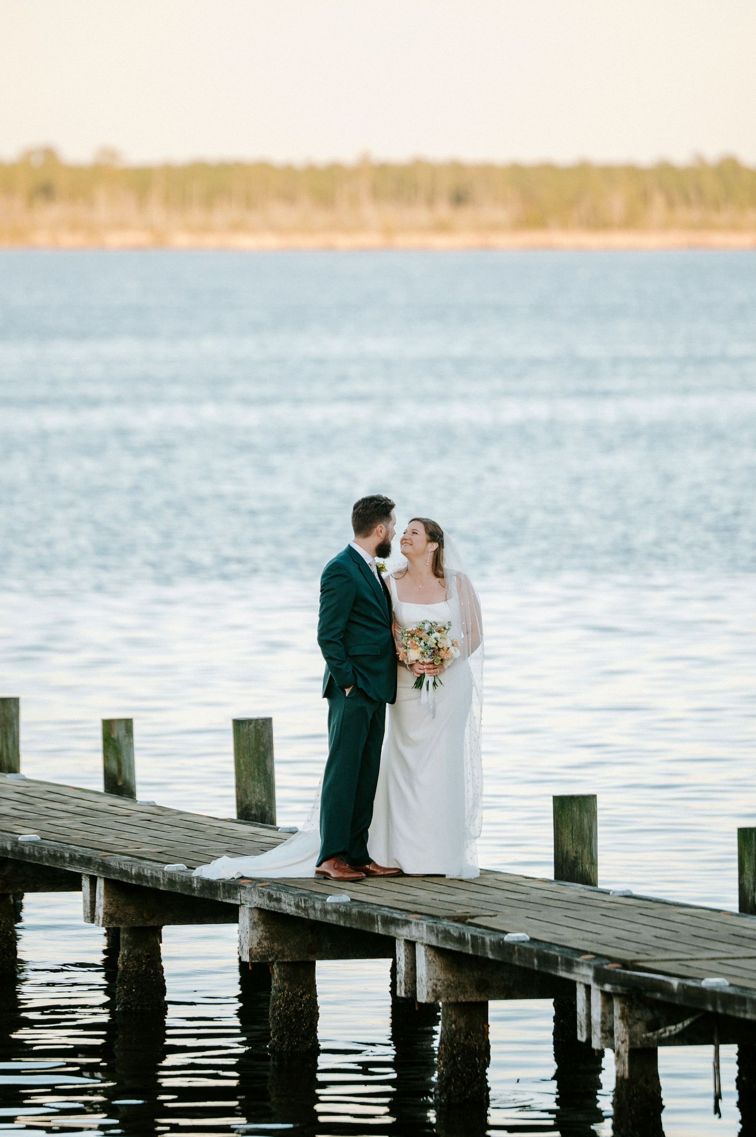 A couple shares a romantic moment on a wooden pier overlooking a serene lake at sunset.