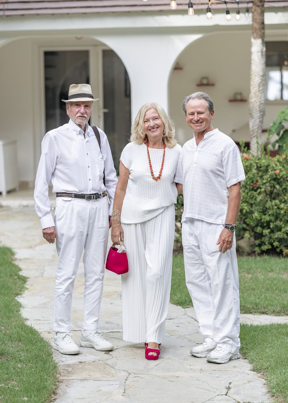 Group of people in white attire walking together on a garden path with one person wearing pink shoes.
