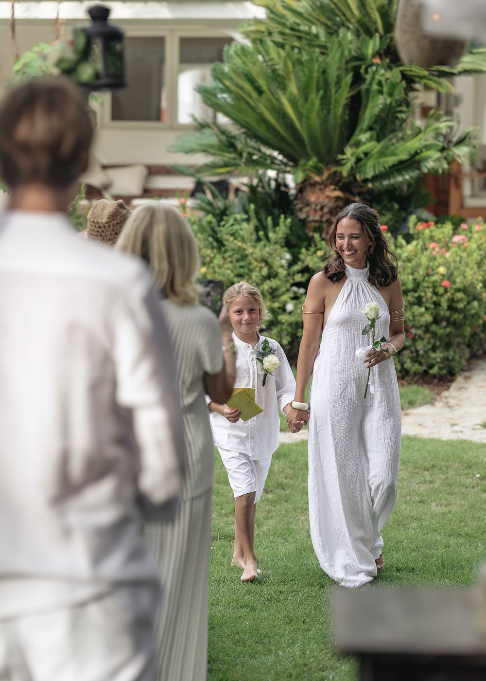 People dressed in white outfits walking through a tropical garden setting.