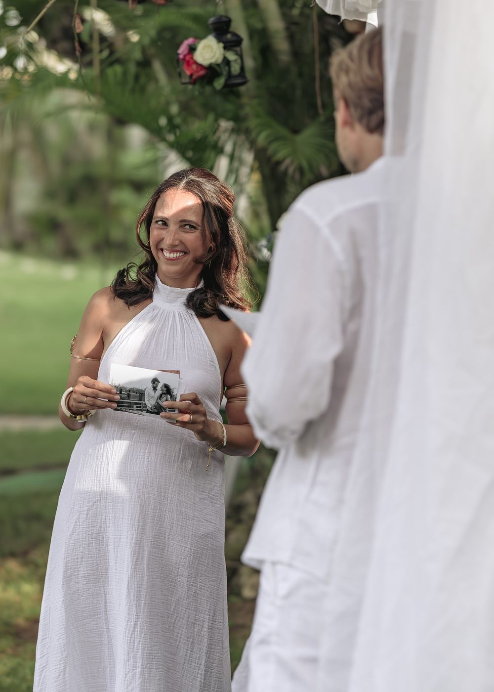 Wedding party members in white attire gathering outdoors in a garden setting.