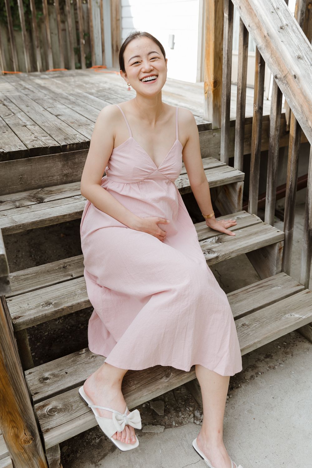 A pink dress and white sandals are showcased while sitting on wooden stairs.