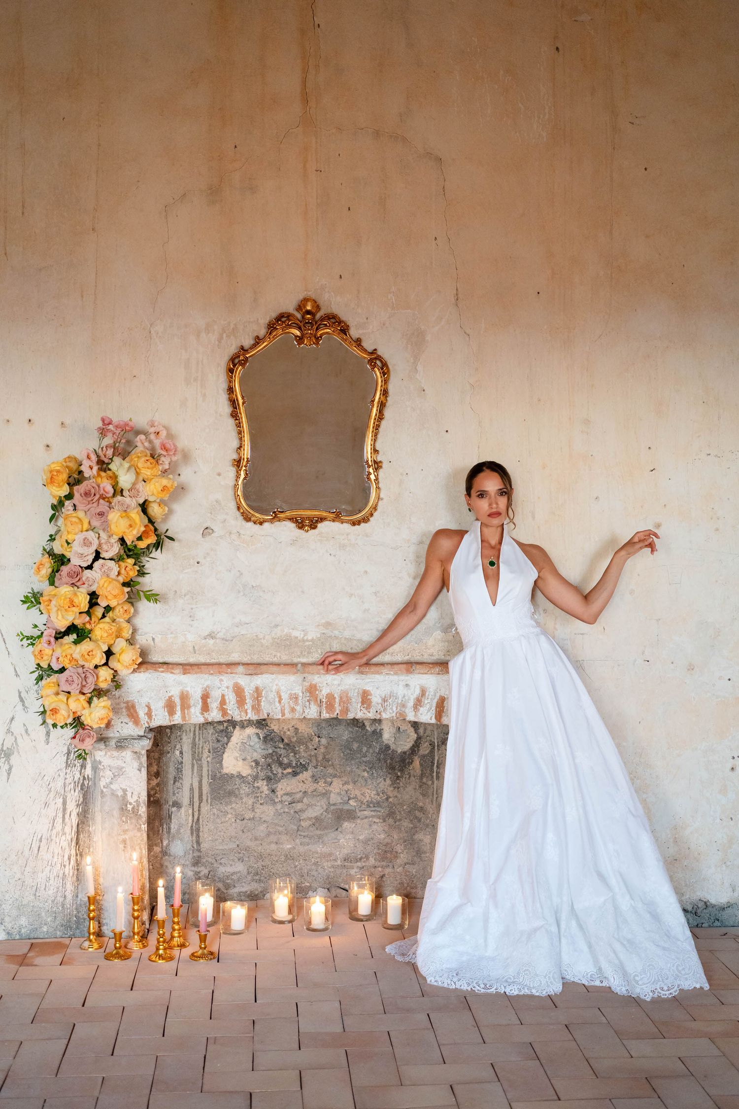 A bride in a white dress poses with vibrant red and pink floral arrangements against a light backdrop.