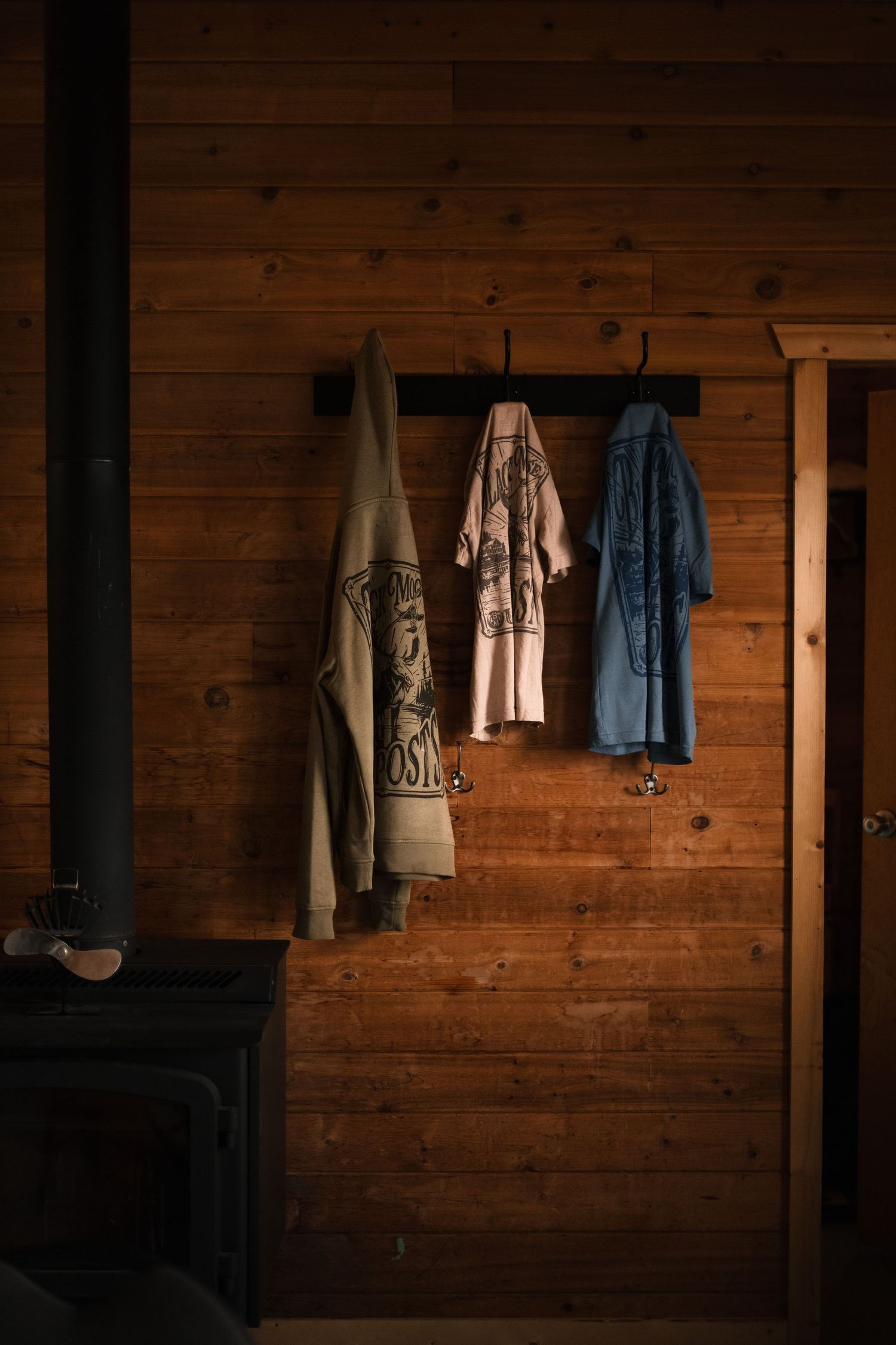 Rustic wooden cabin wall with outdoor clothing and gear hanging on hooks.
