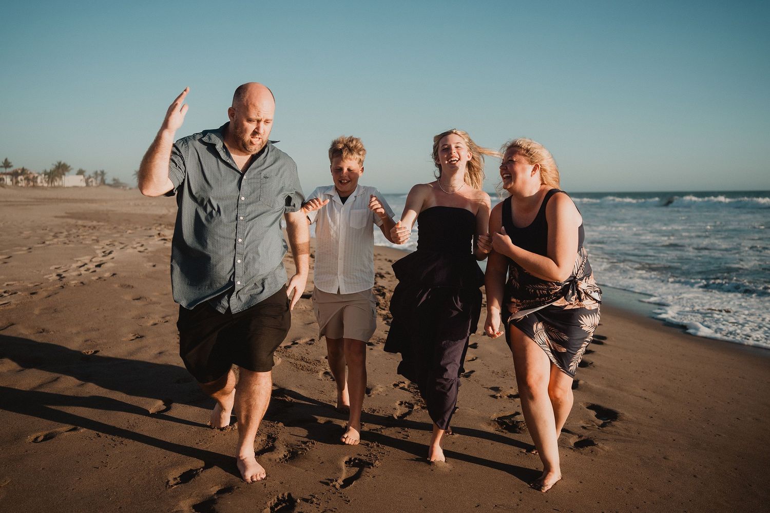 Familia jugando y corriendo junta durante una sesión familiar en la playa de Mazatlán.