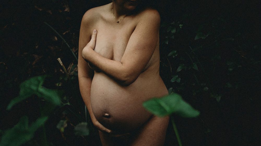 foto colorida grávida Nua na natureza com mãos na barriga durante sessão fotográfica de grávida em Caldas Da Rainha