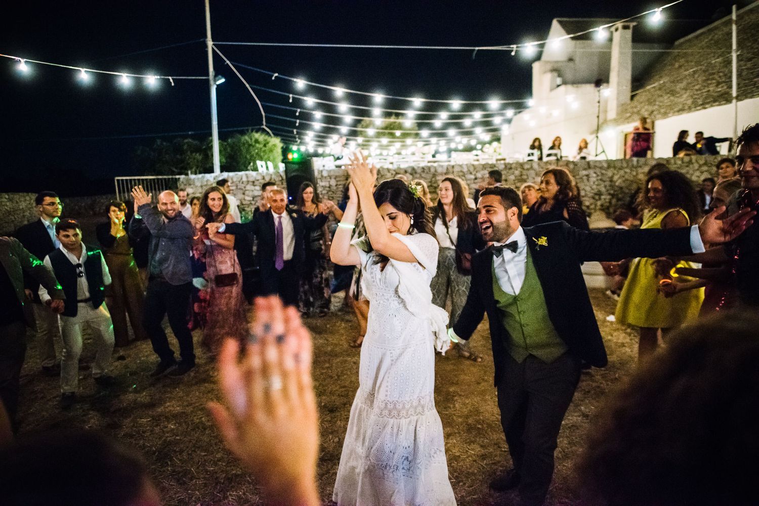 Festive outdoor evening celebration with string lights and dancing on beach.