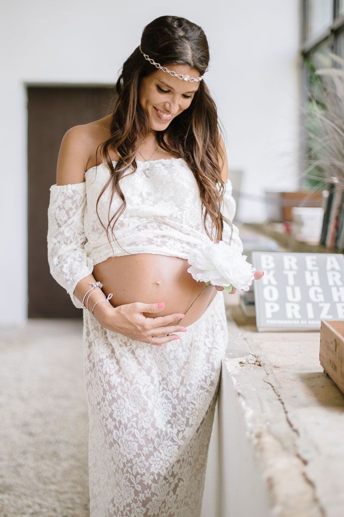 Intimate maternity portrait showing belly in white lace dress by window.