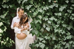 Couple embraces against ivy-covered wall during outdoor maternity photoshoot.
