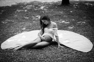 Artistic maternity photo with flowing white fabric spread on ground in black and white.