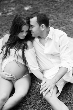 Intimate black and white maternity portrait of couple sitting together outdoors.