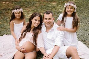 Outdoor family maternity photo with everyone wearing white on a picnic blanket.