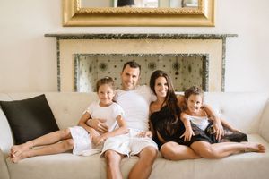 A family lounges together on a white couch beneath a decorative mirror in a casual indoor setting.