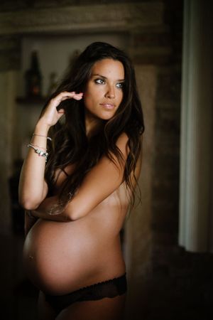An artistic maternity photo capturing an expectant mother in a moody, intimate setting.