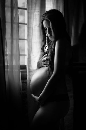 A black and white maternity silhouette by a window creating a dramatic artistic portrait.