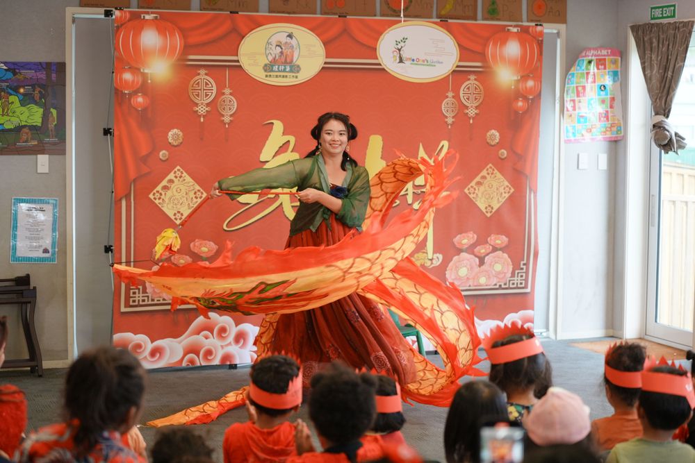 Event photography of a woman in Hanfu interacting with children at a kindergarten New Year party, by an Auckland event photographer.