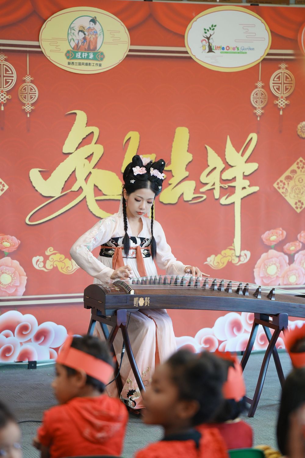 Event photography of a woman in Hanfu interacting with children at a kindergarten New Year party, by an Auckland event photographer.