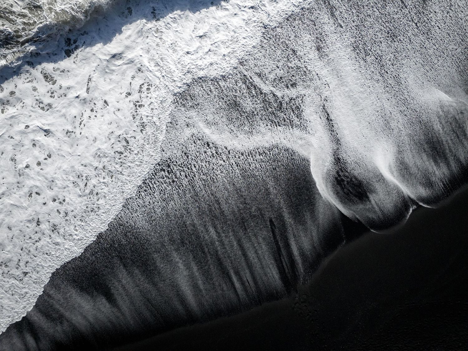 Abstract aerial black and white photograph of ocean waves creating dramatic patterns.