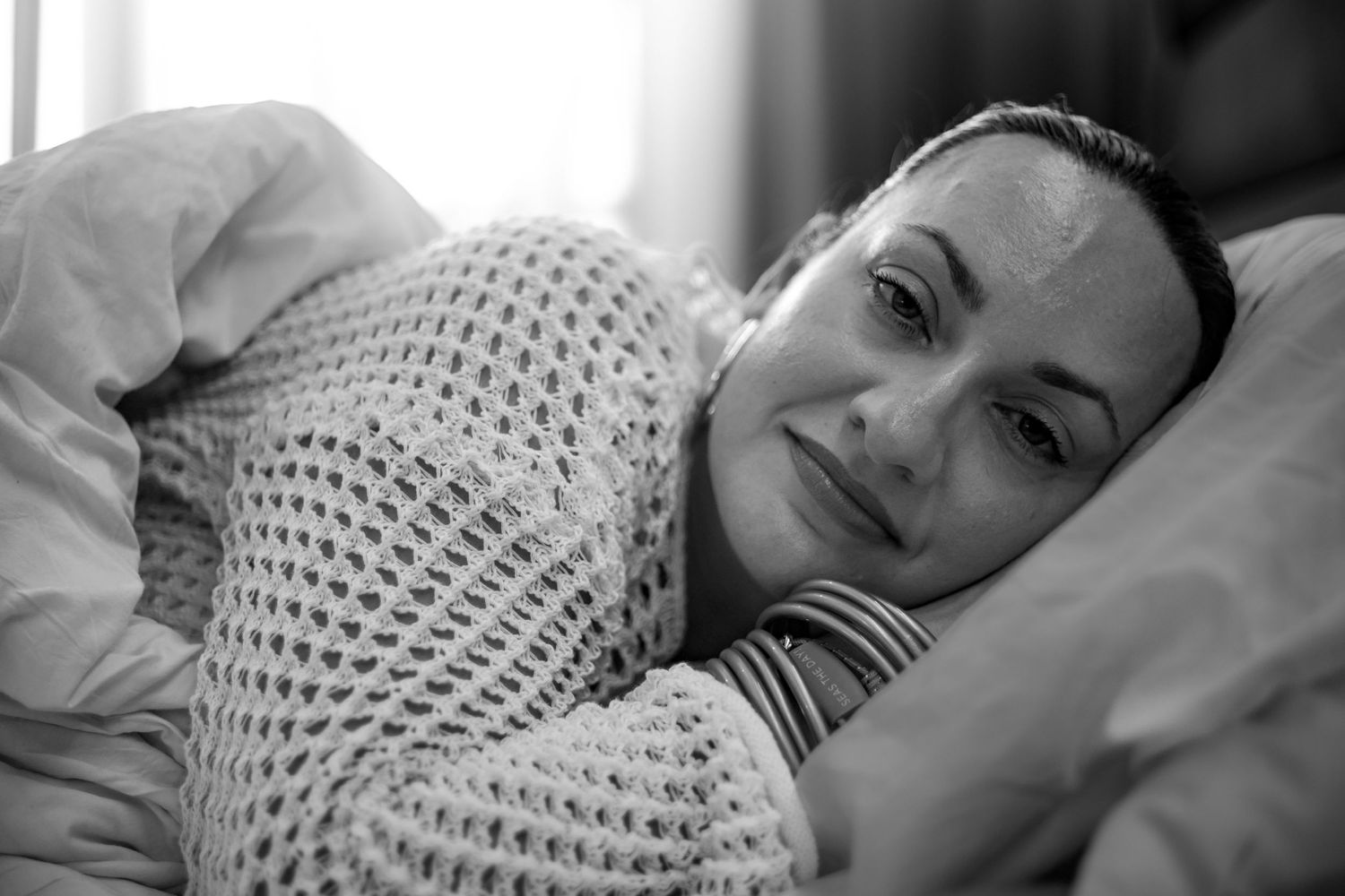 Black and white portrait of person resting on pillow with knit sweater.